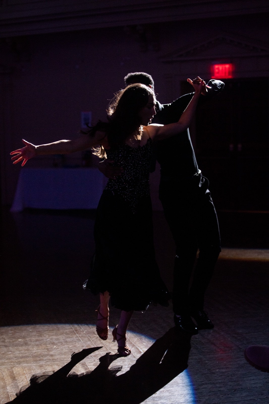 Two dancers in closed hold under a single light.