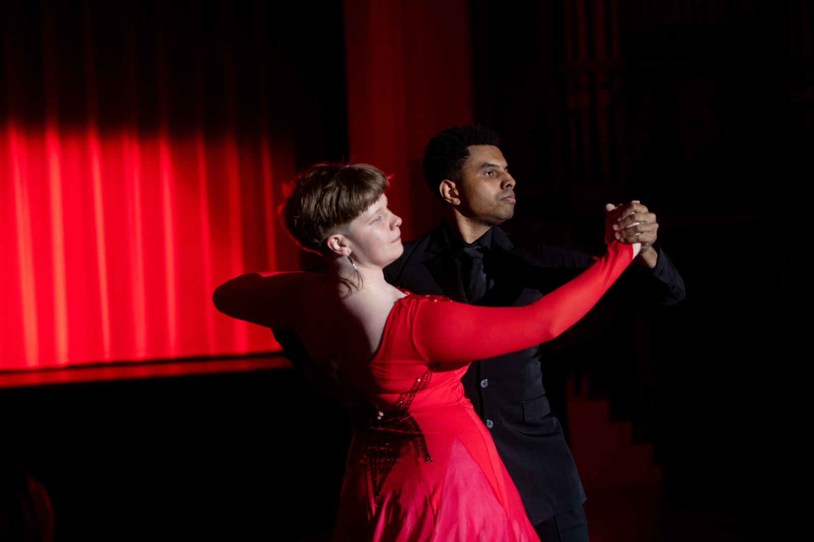 A couple in closed hold against a red curtain.