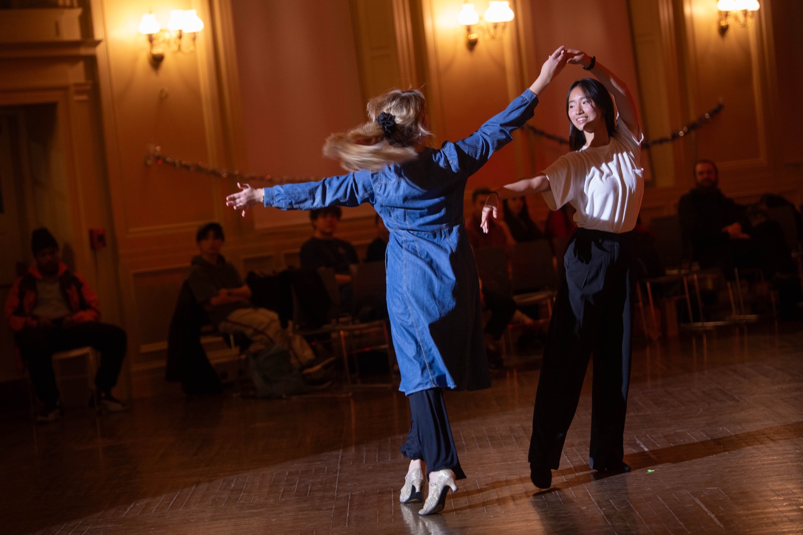 Two dancers in everyday clothes turning in a warm ballroom.